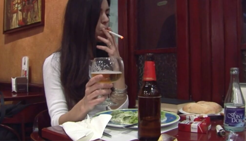 Ana smoking two cigarettes at once in restaurant